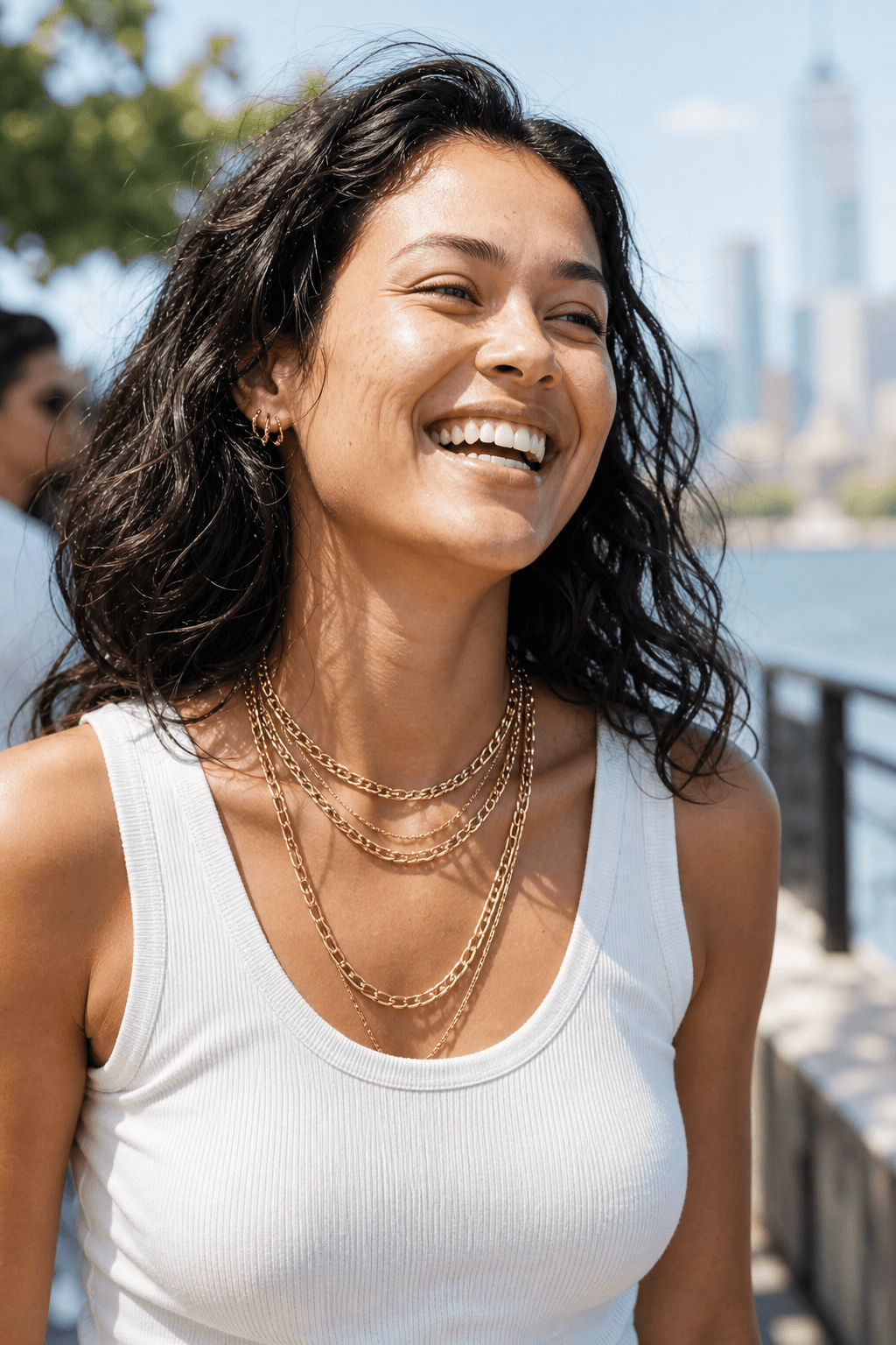 Person laughing in soft daylight wearing layered solid gold jewelry.